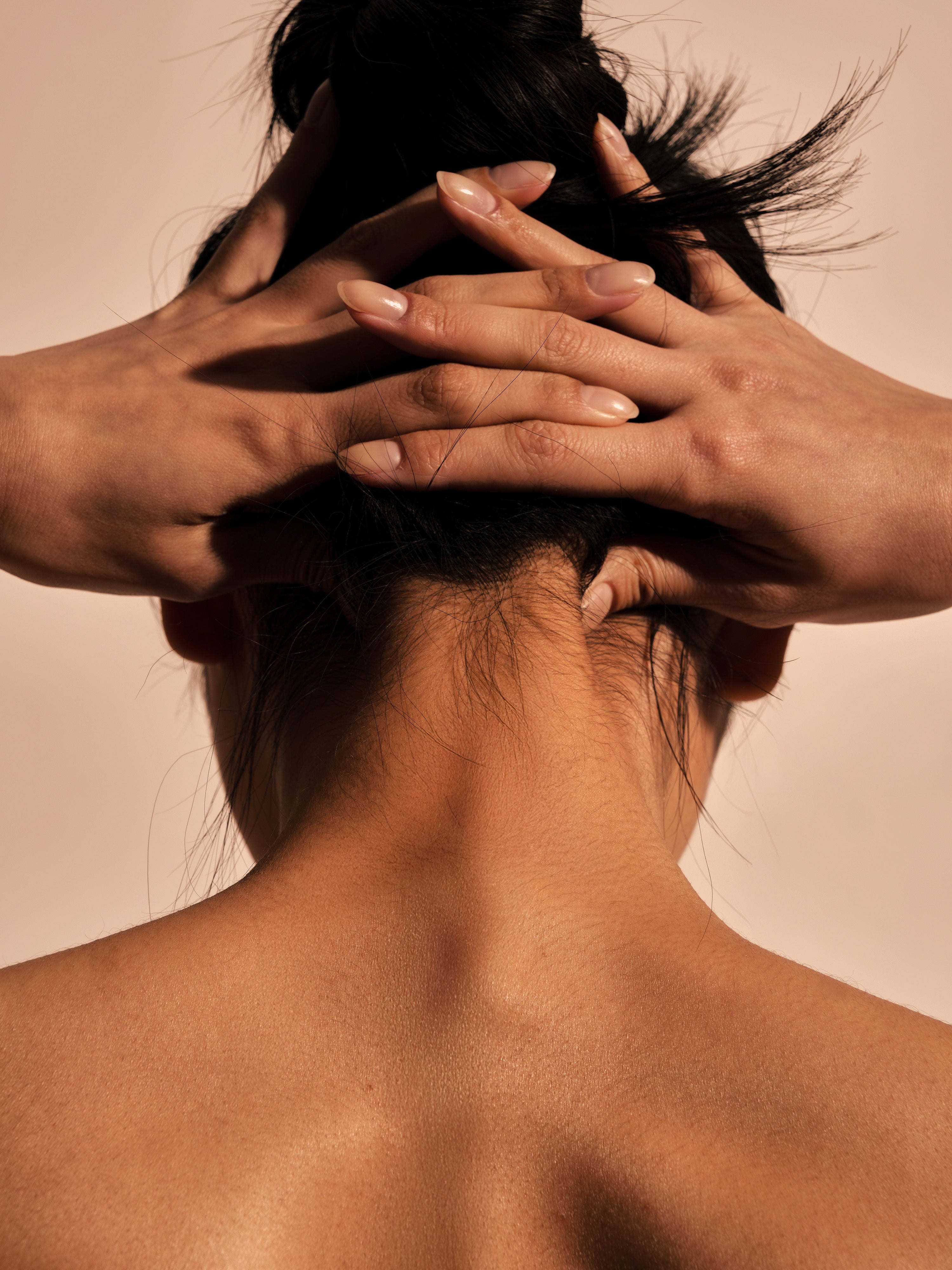 Two hands gripping the back of neck — close-up rear shot expressing neck tension and pain, evocative