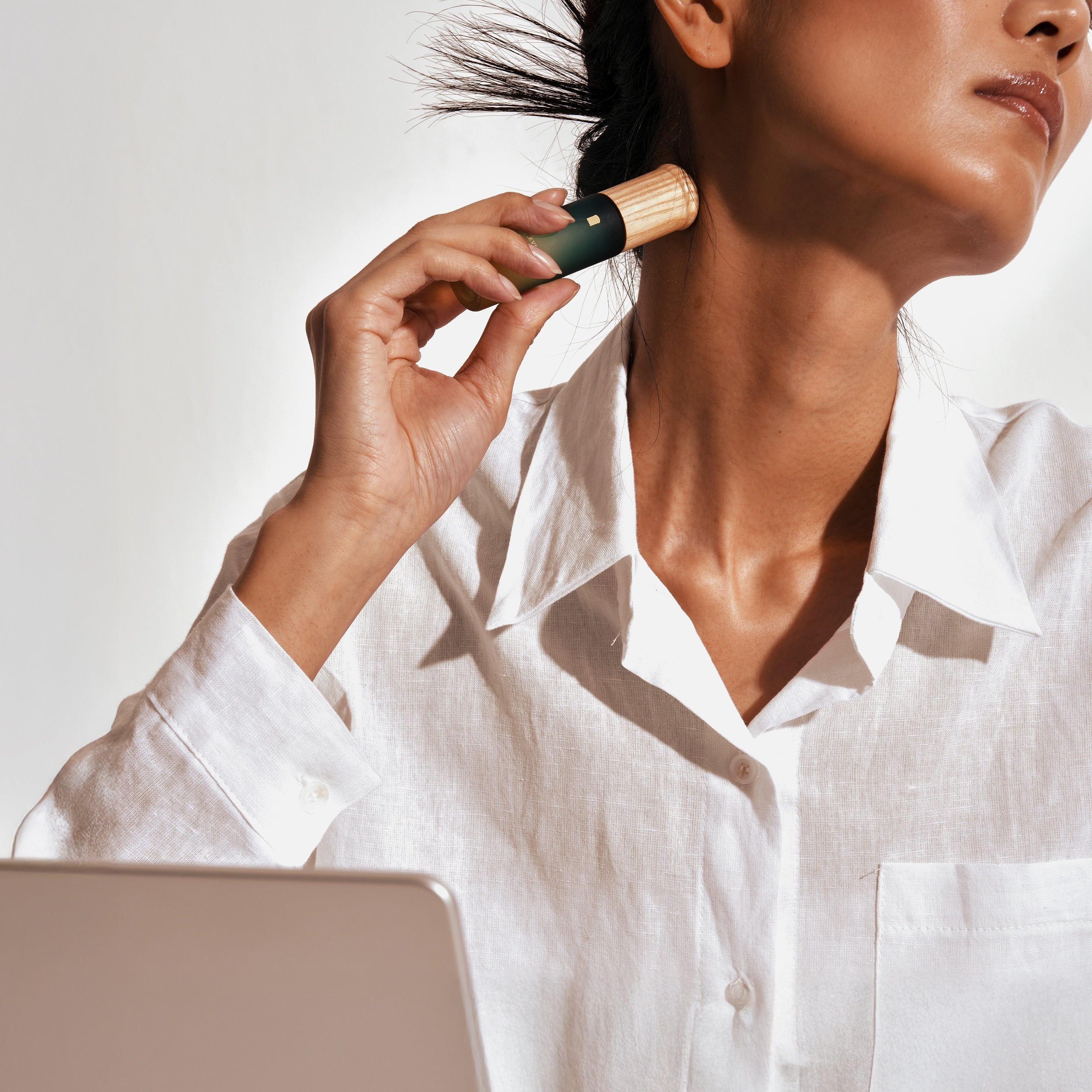 Office scene — person at laptop, neck feeling tight, naturally reaching for the serum on desk