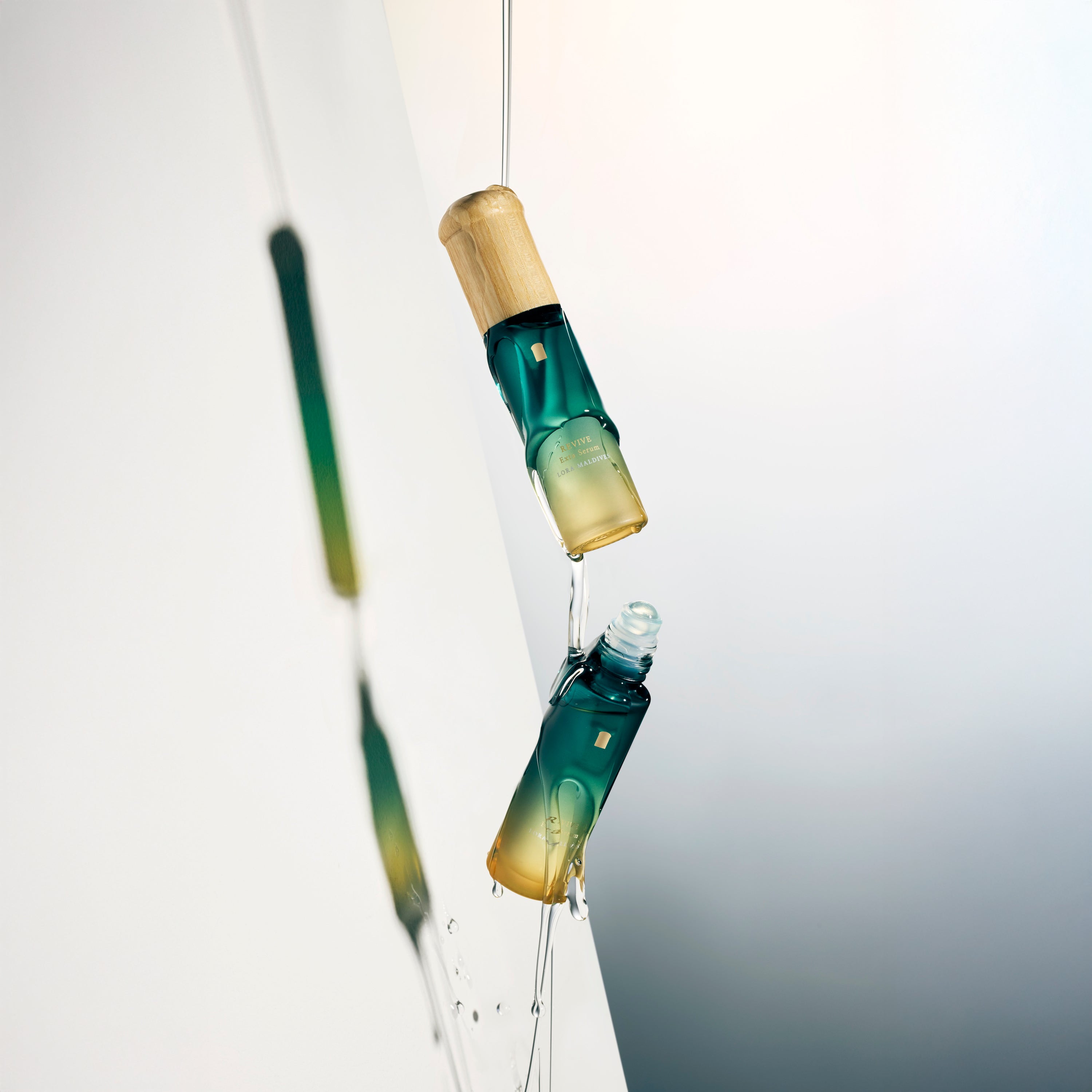 Two Revive Exta Serum bottles tilted — essential oil flowing, sensual product shot, dark background