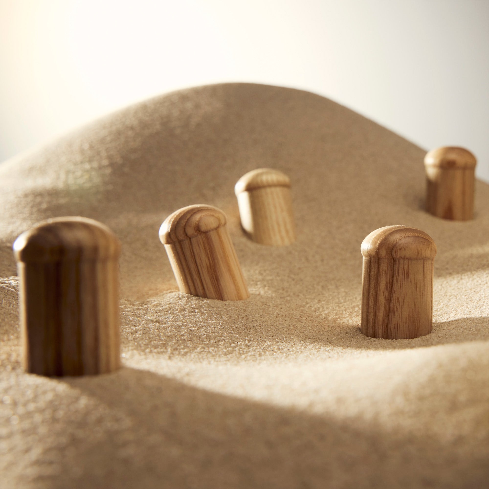 Ash woodcaps on sand — individually carved from premium ash wood woodcap massagers in a row, natural wood grain texture, warm light